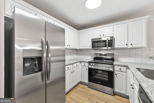kitchen featuring appliances with stainless steel finishes, white cabinetry, and light stone counters