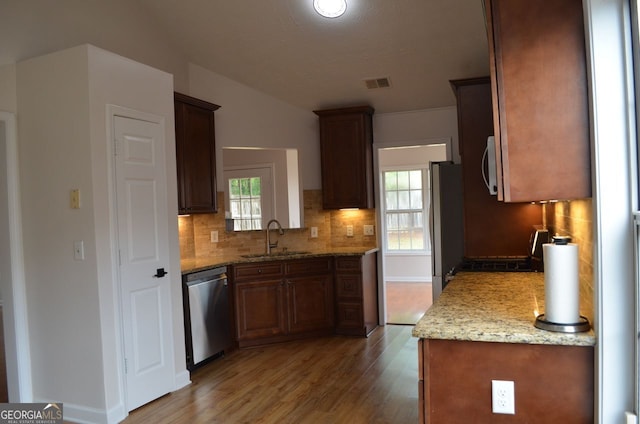 kitchen with appliances with stainless steel finishes, a sink, decorative backsplash, wood finished floors, and plenty of natural light