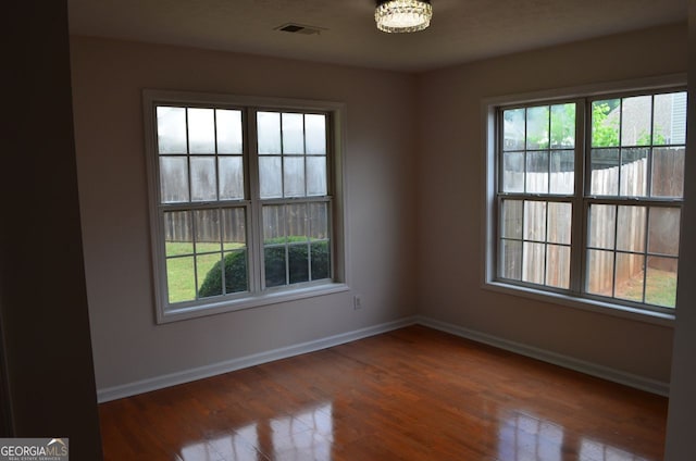 empty room with healthy amount of natural light, baseboards, wood finished floors, and a chandelier