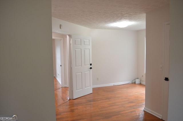 spare room with a textured ceiling, wood finished floors, and baseboards