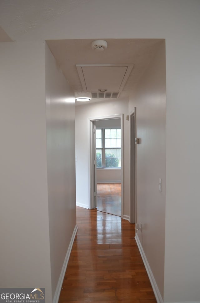hallway featuring wood finished floors, attic access, and baseboards