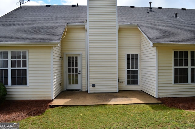 back of house featuring a patio area, a chimney, a shingled roof, and a yard