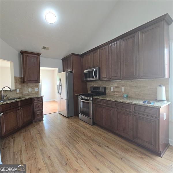 kitchen featuring stainless steel appliances, a sink, backsplash, light wood finished floors, and vaulted ceiling
