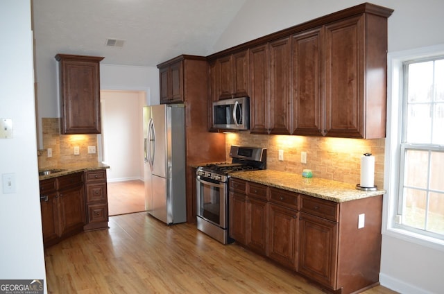 kitchen featuring stainless steel appliances, light wood finished floors, tasteful backsplash, light stone countertops, and vaulted ceiling
