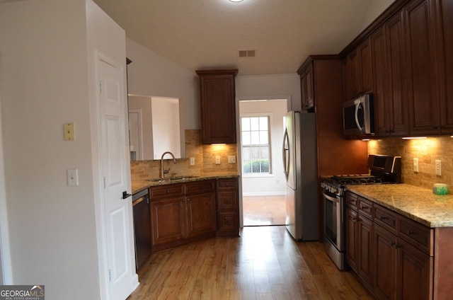 kitchen with stainless steel appliances, a sink, light wood-style floors, light stone countertops, and backsplash
