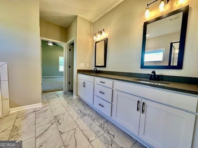 bathroom featuring marble finish floors, baseboards, double vanity, and ceiling fan