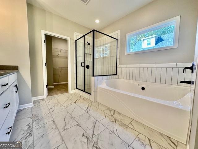 bathroom with a stall shower, a bath, a walk in closet, vanity, and baseboards