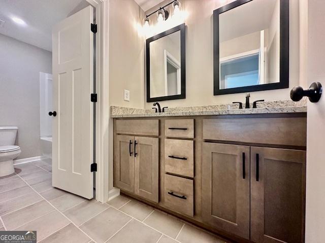 full bath featuring toilet, double vanity, tile patterned floors, a bathtub, and baseboards