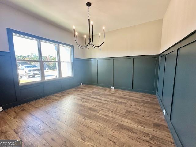 unfurnished dining area with a decorative wall, a chandelier, light wood-type flooring, and a wainscoted wall