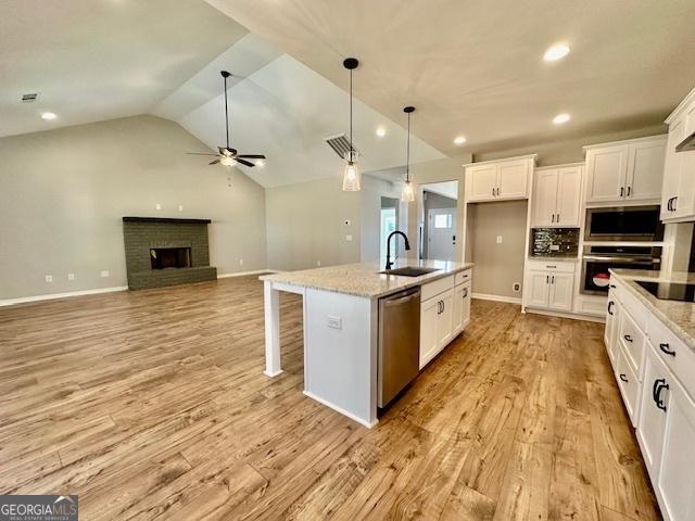 kitchen with a sink, stainless steel appliances, a ceiling fan, white cabinets, and vaulted ceiling