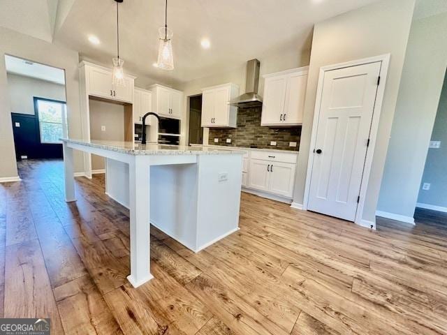 kitchen featuring wall chimney range hood, light wood-type flooring, white cabinets, decorative backsplash, and recessed lighting