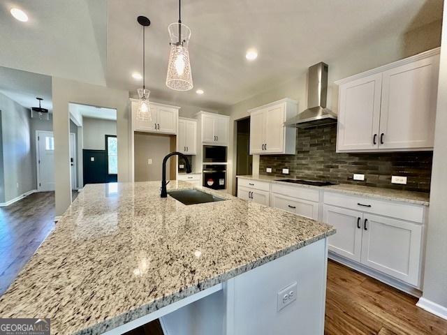 kitchen featuring wall chimney exhaust hood, a sink, decorative backsplash, white cabinetry, and a large island
