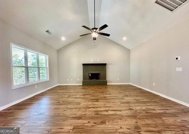 unfurnished living room with wood finished floors, ceiling fan, a brick fireplace, lofted ceiling, and baseboards
