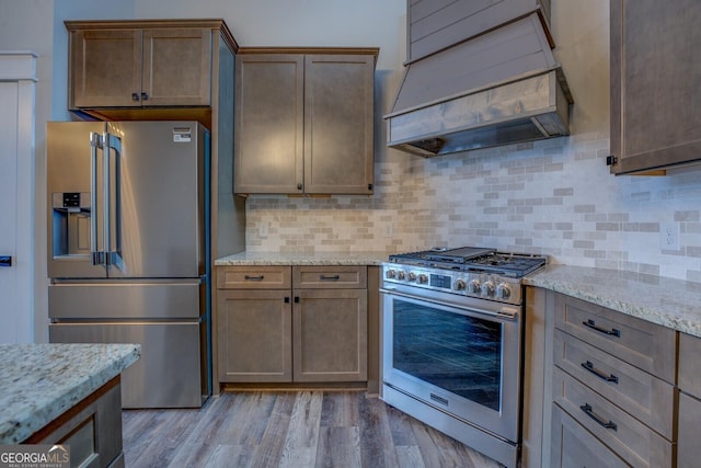 141G Lake Pines Rd, Jackson, GA 30233 - kitchen featuring appliances with stainless steel finishes, custom exhaust hood, backsplash, light stone counters, and light wood-style floors