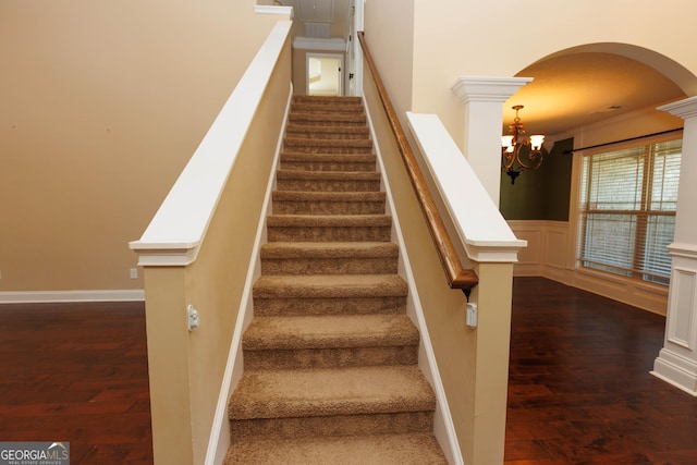 stairs featuring wood finished floors, a chandelier, arched walkways, and wainscoting