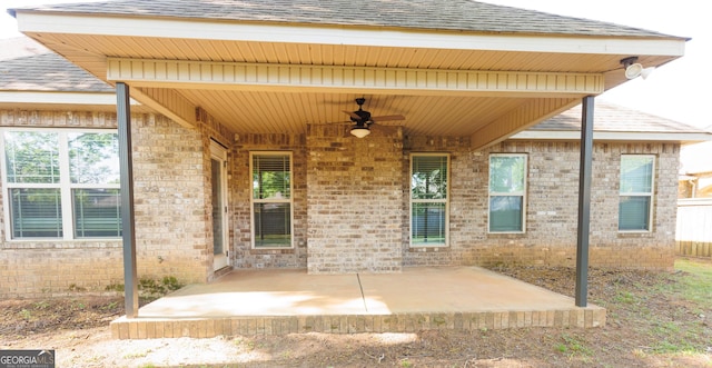 entrance to property with ceiling fan, a patio area, a shingled roof, and brick siding