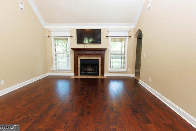 unfurnished living room featuring ornamental molding, arched walkways, dark wood-style floors, a fireplace, and baseboards