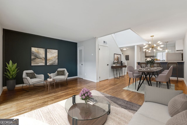 living room featuring an accent wall, a chandelier, light wood-style floors, and baseboards