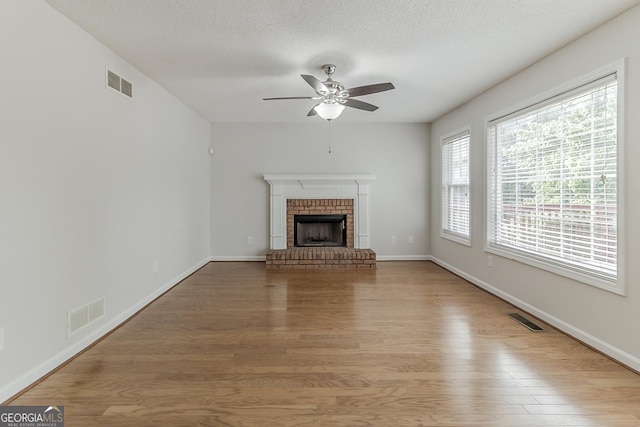 3717 Lockerbie Ln, Powder Springs, GA 30127 - unfurnished living room featuring ceiling fan, plenty of natural light, light wood-style floors, a brick fireplace, and a textured ceiling