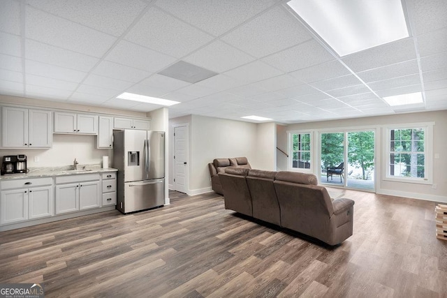 living area with wood finished floors, a paneled ceiling, and baseboards