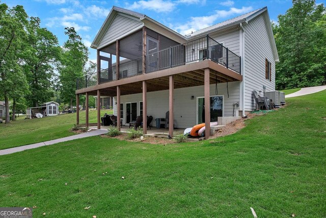 back of property featuring a lawn, a sunroom, a patio area, a wooden deck, and a shed