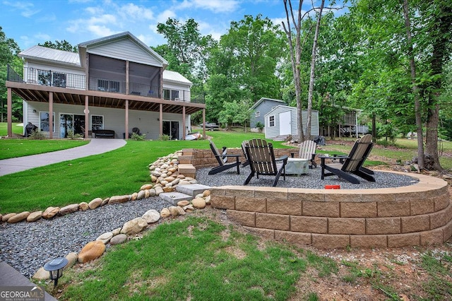 view of grassy yard featuring an outdoor fire pit, a deck, an outbuilding, a storage unit, and a patio