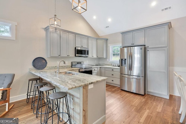kitchen featuring appliances with stainless steel finishes, a sink, a peninsula, a kitchen bar, and light wood finished floors