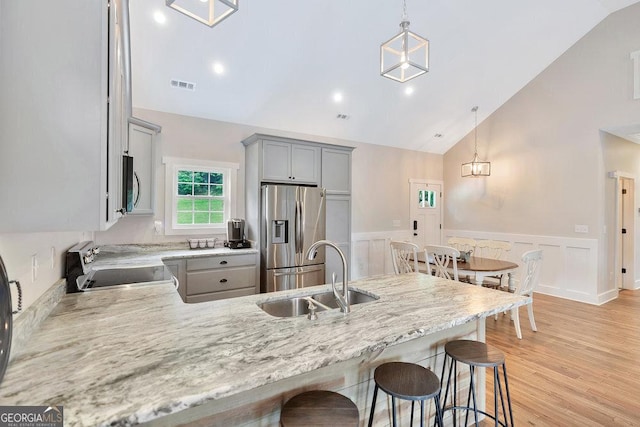 kitchen with appliances with stainless steel finishes, a sink, gray cabinetry, a peninsula, and a wainscoted wall