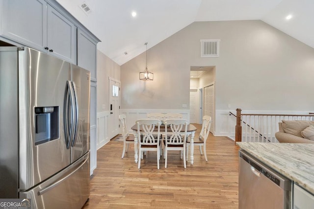 kitchen with appliances with stainless steel finishes, high vaulted ceiling, wainscoting, light wood-type flooring, and light stone counters
