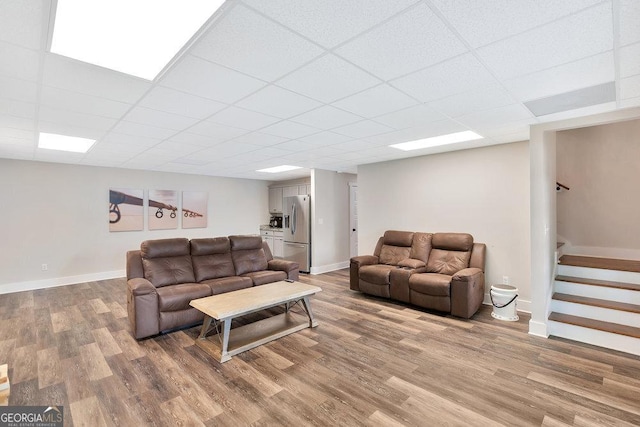 living area with light wood-type flooring, stairway, baseboards, and a drop ceiling