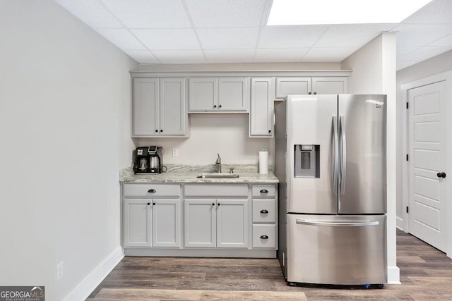 kitchen featuring stainless steel fridge with ice dispenser, a sink, a drop ceiling, wood finished floors, and light stone counters