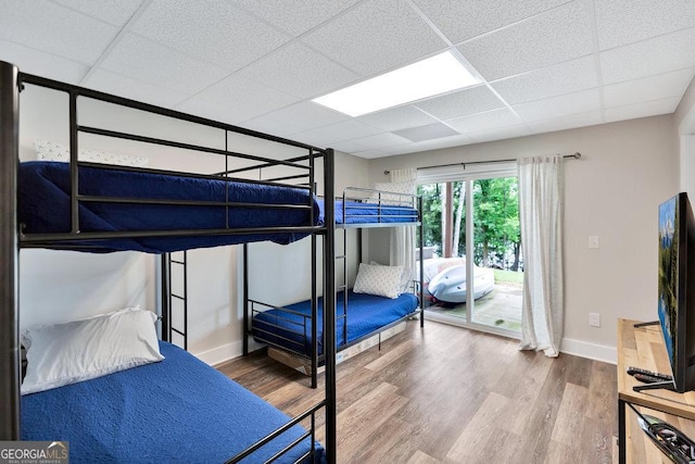bedroom featuring wood finished floors, a drop ceiling, access to outside, and baseboards