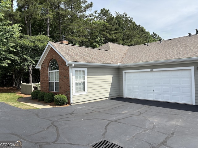 view of property exterior with driveway, roof with shingles, an attached garage, brick siding, and a chimney