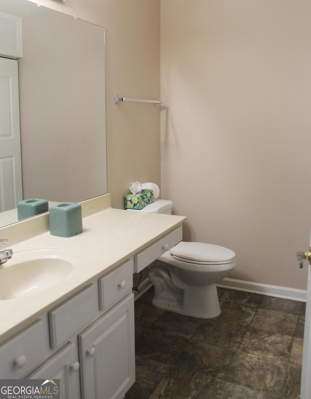 bathroom featuring vanity, toilet, baseboards, and stone finish floors