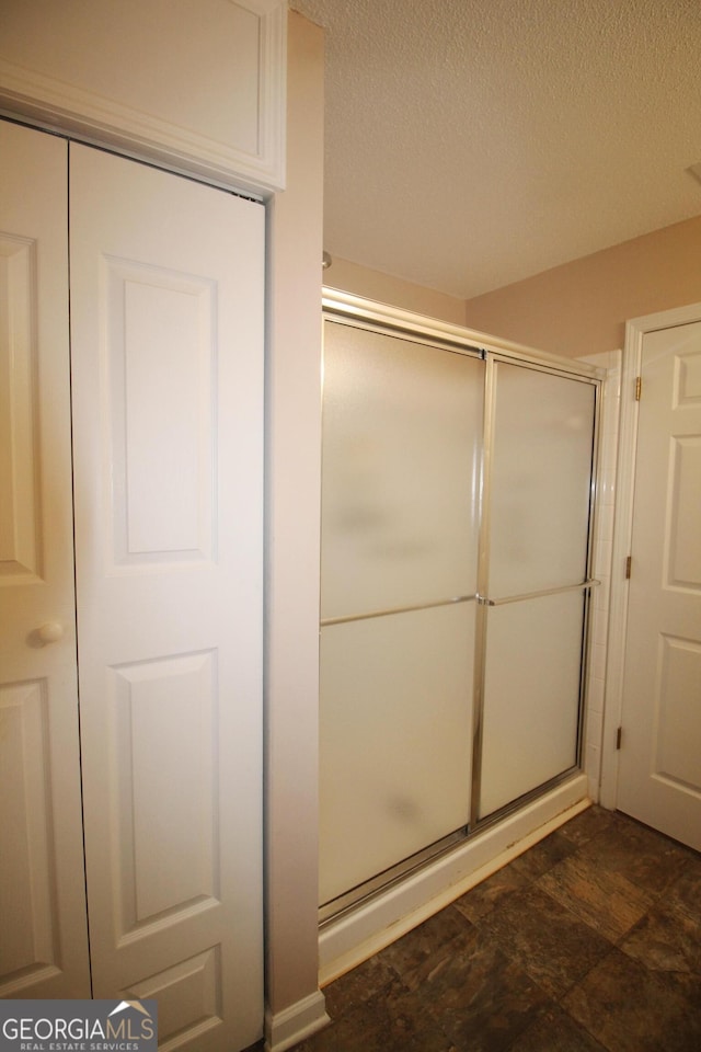 full bath with a shower stall, a textured ceiling, and stone finish flooring