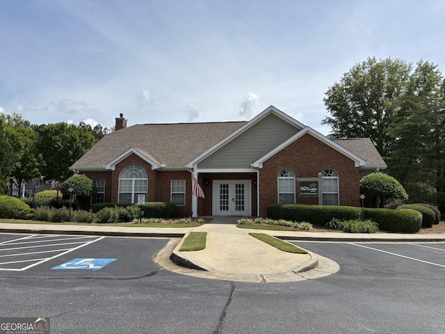 view of front of home featuring french doors, a chimney, uncovered parking, and brick siding
