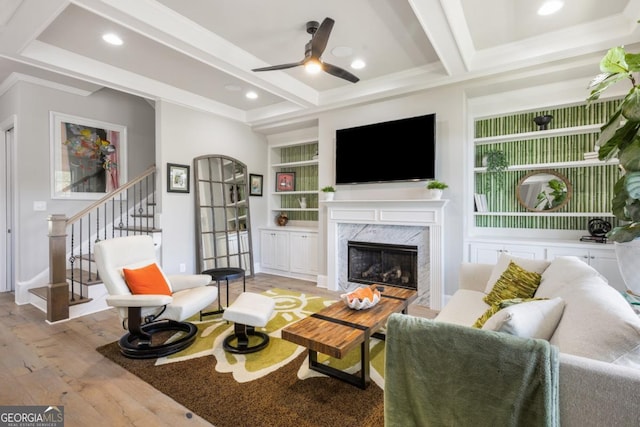 living area with light wood finished floors, beamed ceiling, ceiling fan, a premium fireplace, and stairway
