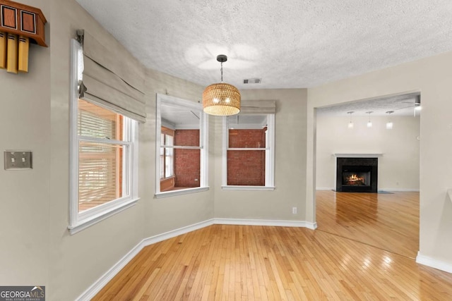 2620 Dr Bramblett Rd, Cumming, GA 30028 - unfurnished dining area featuring light wood-style flooring, baseboards, a warm lit fireplace, and a textured ceiling