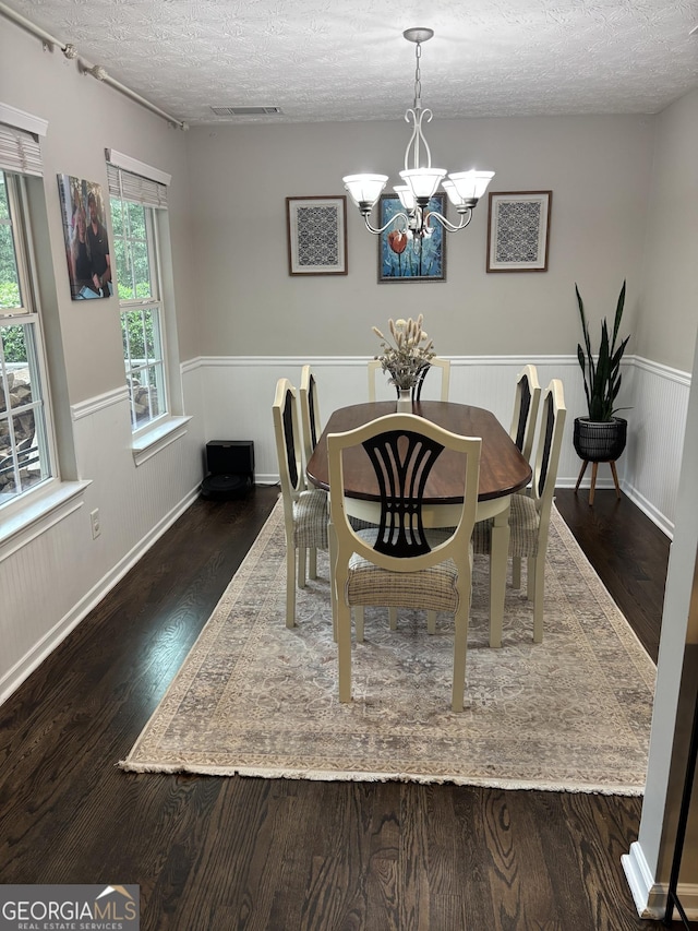 dining room with a chandelier, wood finished floors, wainscoting, and a textured ceiling