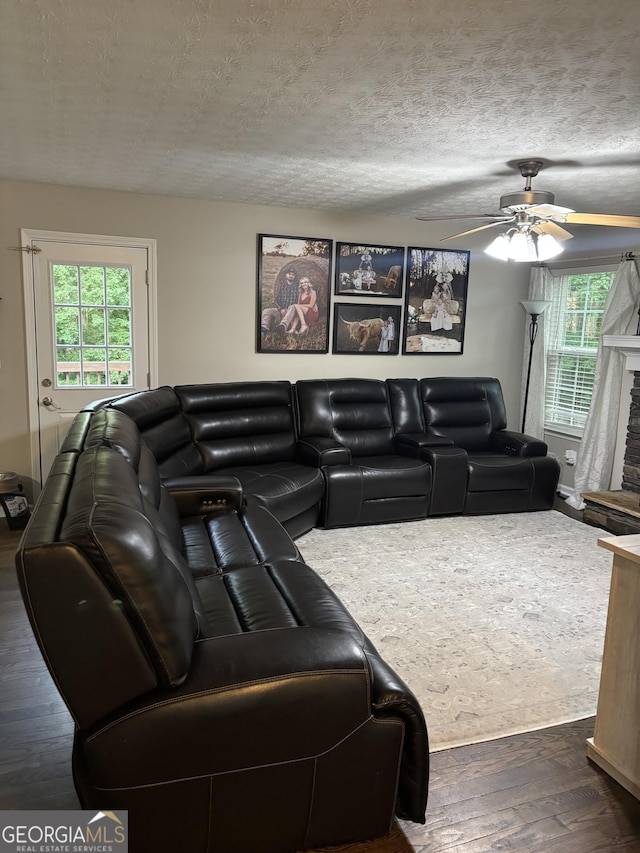 living area with dark wood-style floors, ceiling fan, healthy amount of natural light, a textured ceiling, and a fireplace