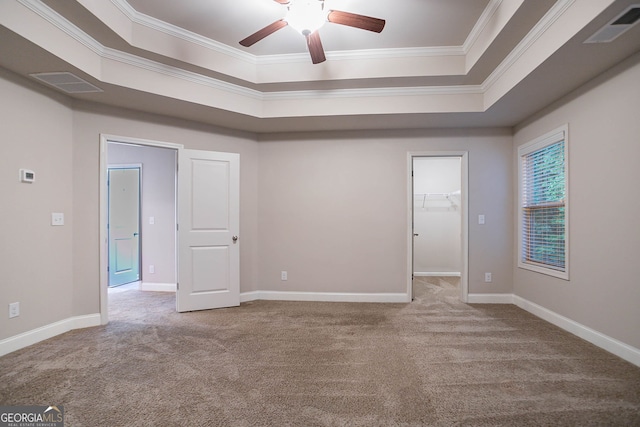 carpeted spare room featuring a tray ceiling, crown molding, ceiling fan, and baseboards