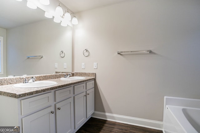 full bathroom with baseboards, wood finished floors, double vanity, and a bathtub