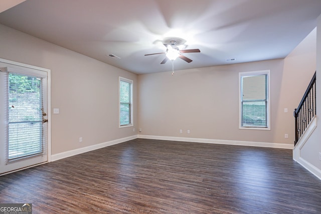 unfurnished living room with a ceiling fan, healthy amount of natural light, dark wood-style flooring, and stairway