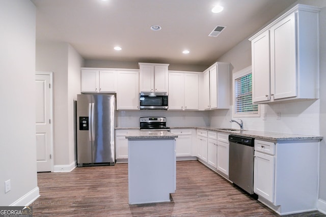 kitchen with stainless steel appliances, a sink, wood finished floors, backsplash, and white cabinets