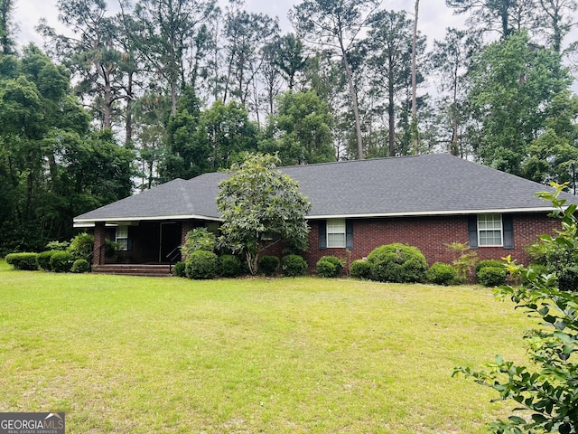 ranch-style home with a front yard, roof with shingles, view of wooded area, and brick siding