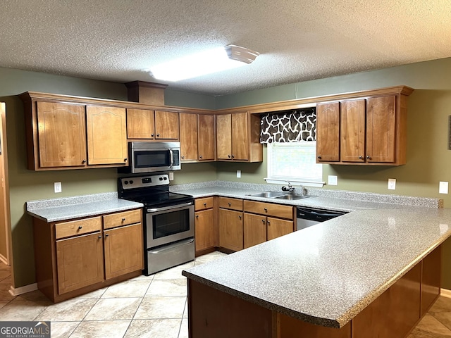 kitchen with appliances with stainless steel finishes, a sink, a peninsula, brown cabinets, and a textured ceiling