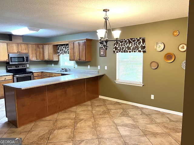 kitchen with appliances with stainless steel finishes, a peninsula, light countertops, healthy amount of natural light, and a textured ceiling