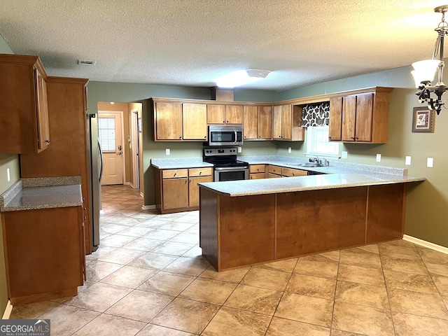 kitchen with stainless steel appliances, a peninsula, a sink, baseboards, and brown cabinetry