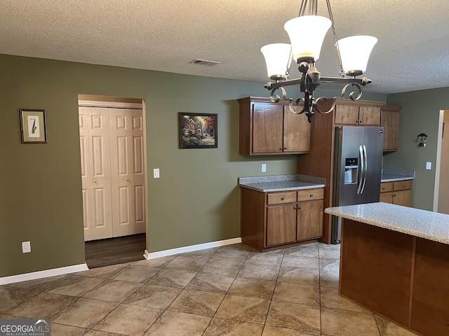 kitchen with stainless steel fridge, a textured ceiling, a chandelier, light countertops, and pendant lighting