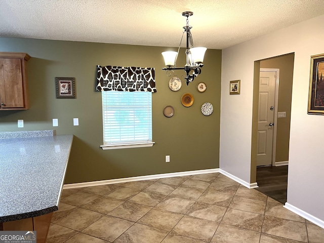 unfurnished dining area with a chandelier, a textured ceiling, light tile patterned floors, and baseboards